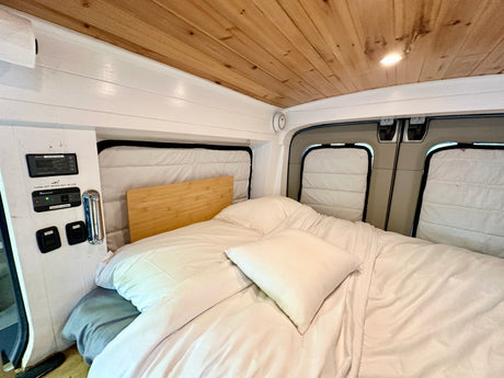 An inviting RV rental bedroom with white bedding, wooden ceiling, and a control panel for lighting and water pump.
