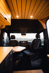 This RV rental features a modern van interior with swivel seats, a table, and warm wooden ceiling lights, perfect for travel.