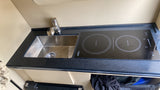 Compact kitchenette in an RV rental featuring a stainless steel sink, faucet, and two-burner induction cooktop on a dark counter.