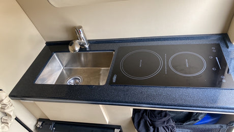 Compact kitchenette in an RV rental featuring a stainless steel sink, faucet, and two-burner induction cooktop on a dark counter.