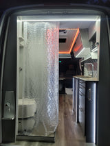 Inside a sleek rv rental: a well-lit shower with clear curtain and a compact kitchen with modern cabinetry and accent lighting.