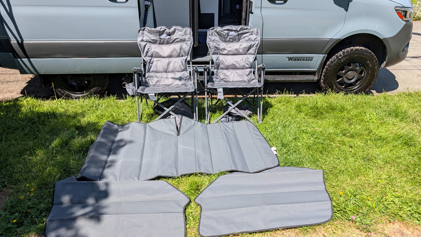 RV rental: Light gray camper van, two padded folding chairs, and window sun shades on green grass.
