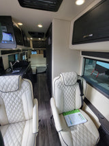 Step inside this plush RV rental featuring cream quilted leather seats, dark wood trim, and a modern control panel.