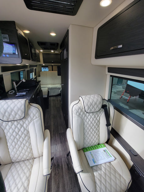 Step inside this plush RV rental featuring cream quilted leather seats, dark wood trim, and a modern control panel.