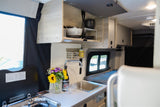 Well-equipped rv rental interior: compact kitchen galley with sink, stove, overhead storage, and flowers on the counter.