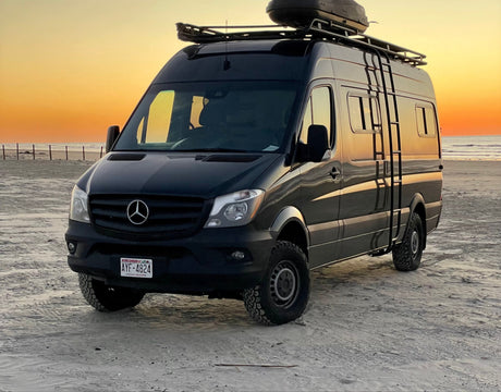 Black Mercedes Sprinter camper van on a sandy beach at sunset, ideal for an RV rental adventure.