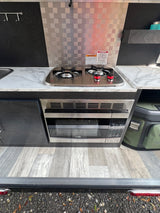 This RV rental kitchen features a two-burner gas cooktop, built-in microwave, and marble-look countertops, with a metallic backsplash.