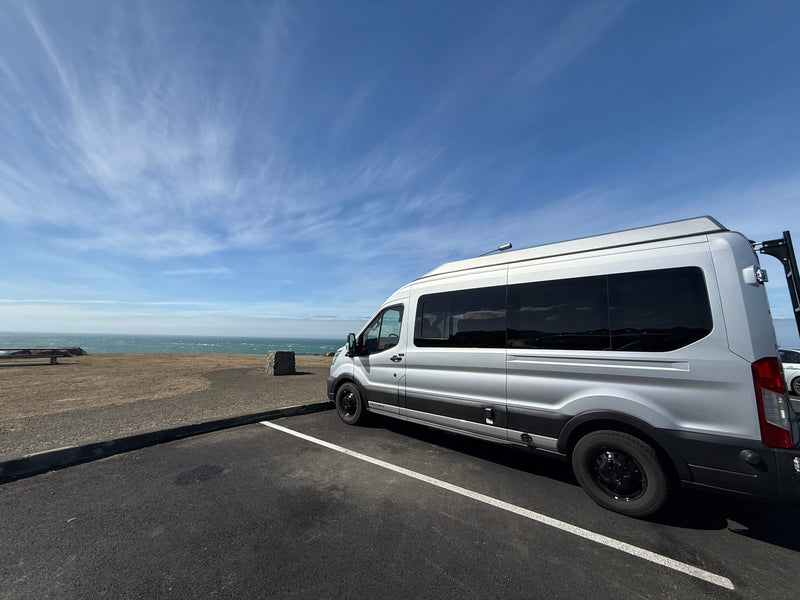 This silver RV rental is parked coastside. A camper van overlooks the vast blue ocean under a vibrant sky, ready for adventure. — photo 7