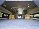 Spacious RV rental camper van interior. View from the large bed shows overhead storage, windows, and a compact kitchen.