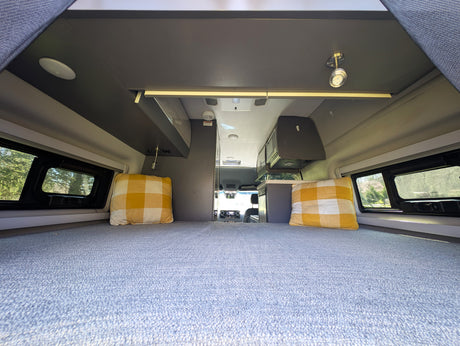 Spacious RV rental camper van interior. View from the large bed shows overhead storage, windows, and a compact kitchen.