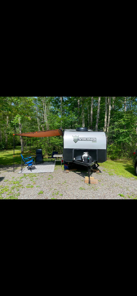 RV rental: Viking Max travel trailer with awning, chairs, and table at a sunny, wooded campsite.