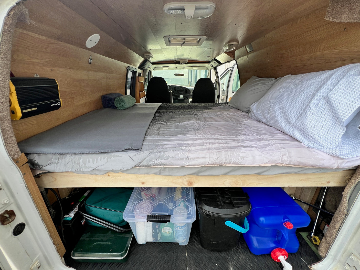 This RV rental shows a comfy camper van interior with a bed, power inverter, and organized under-bed storage, ideal for mobile adventures.