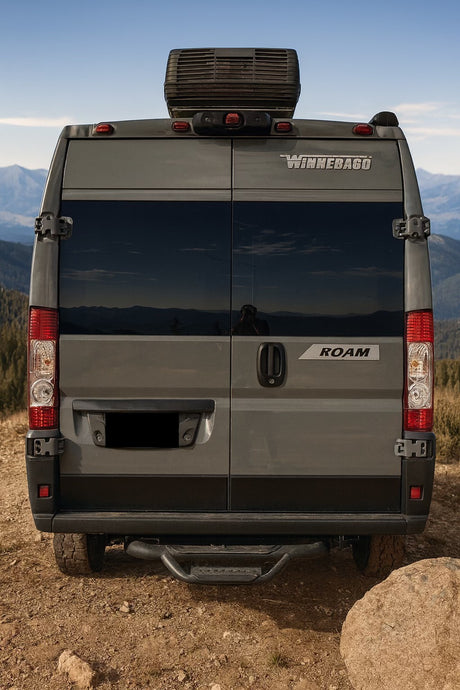 Grey Winnebago Roam RV rental's rear view, parked on a mountain trail. Ideal for adventure, travel, and van life.