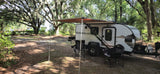 Shady Bushwhacker camper RV rental under live oaks. Perfect camping setup with awning, chairs, and outdoor kitchen.
