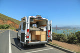 White RV rental camper van with open doors, revealing bed & storage, parked overlooking Golden Gate Bridge.