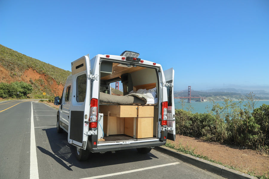 White RV rental camper van with open doors, revealing bed & storage, parked overlooking Golden Gate Bridge.