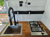 RV rental: well-equipped kitchenette features a modern sink, pull-down faucet, gas stove, and controls for tank heaters. Compact & functional.