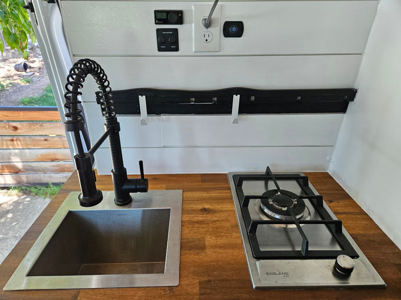 RV rental: well-equipped kitchenette features a modern sink, pull-down faucet, gas stove, and controls for tank heaters. Compact & functional. — photo 2