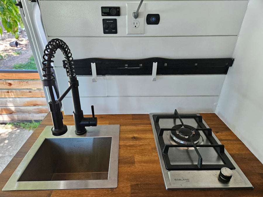 RV rental: well-equipped kitchenette features a modern sink, pull-down faucet, gas stove, and controls for tank heaters. Compact & functional.