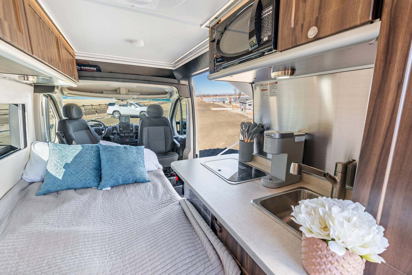 An RV rental's inviting interior with a comfortable bed, full kitchen including microwave and coffee maker, and driver's seat.