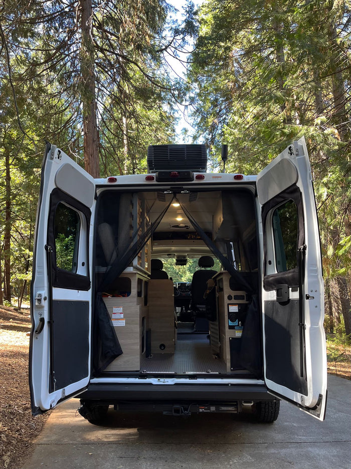 RV rental's rear doors open in a sunny forest, showcasing its cozy interior ready for adventure and travel.