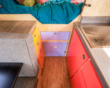 Colorful RV rental interior: cozy bed, compact kitchen with sink, bright storage cabinets, and comfortable seating.