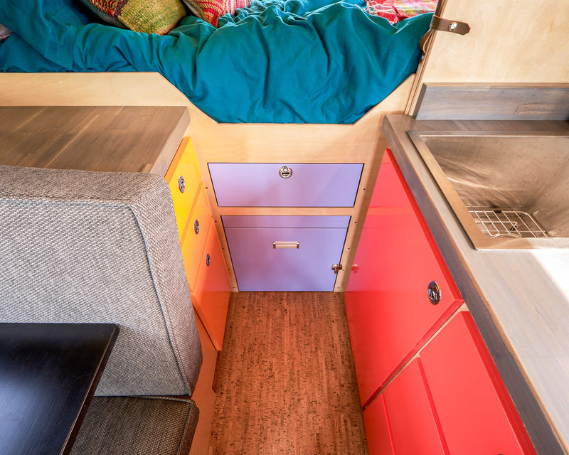 Colorful RV rental interior: cozy bed, compact kitchen with sink, bright storage cabinets, and comfortable seating. — photo 16