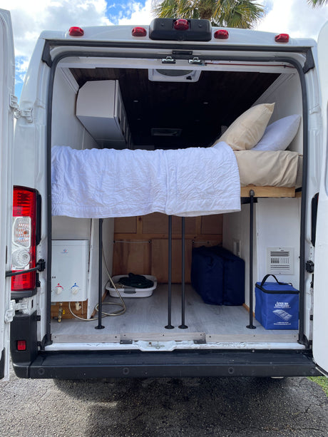 RV rental: Rear view of a camper van interior, featuring a raised bed, under-bed storage, and an EcoTemp water heater.