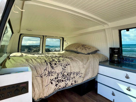 RV rental camper van interior: Features a cozy bed with ocean views, coffee maker, and power panel for your comfort.