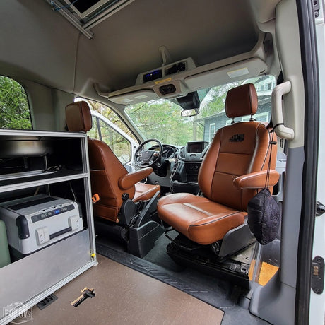 RV rental: Inside a customized camper van with brown swiveling seats, a compact galley, and a portable fridge.