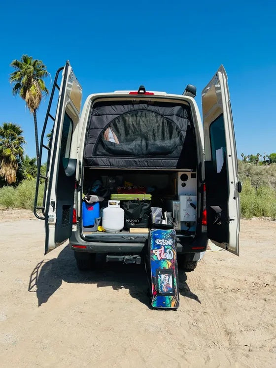 Adventure awaits! This RV rental is packed for van life, showing a functional interior & gear like a surfboard under a clear sky.