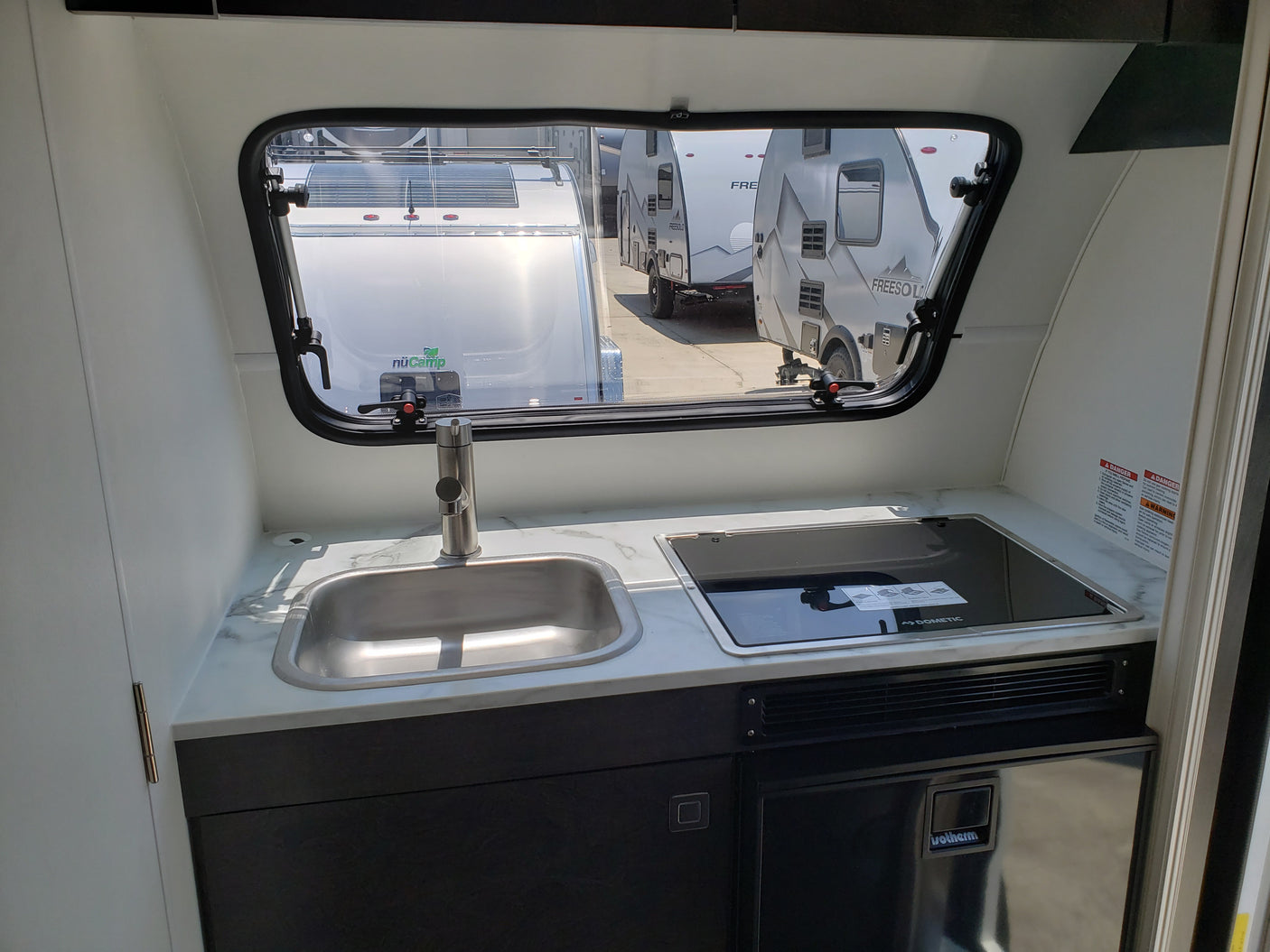 Inside a compact RV rental: a modern galley with a sink, Dometic cooktop, and Isotherm fridge.