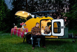 Cozy RV rental adventure: A couple enjoys champagne by their yellow teardrop camper at dusk, ideal for glamping.