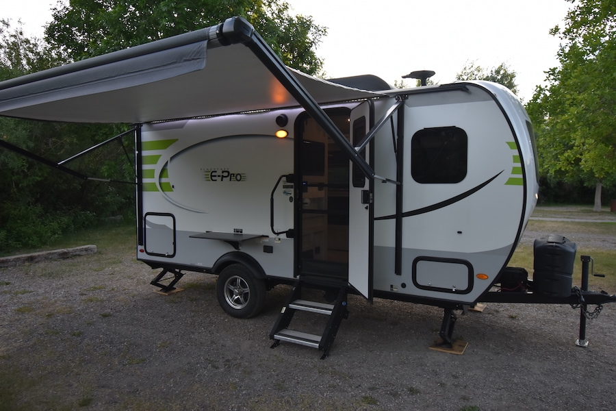 This Flagstaff E-Pro travel trailer RV rental is set up at a campsite with its awning extended and door open, perfect for camping. — photo 6