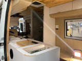 An RV rental conversion in progress, showcasing custom wooden and white interior cabinetry, a window, and storage elements.