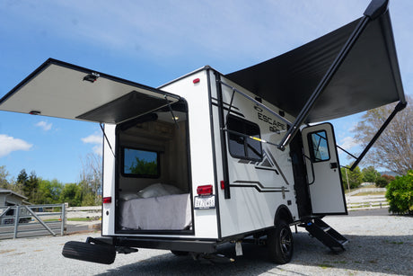 White RV rental with its rear door open revealing a bed inside, and a side awning extended.