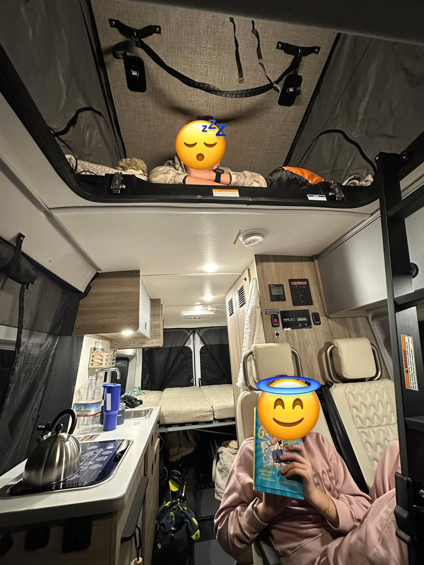 Cozy rv rental interior: one person sleeps in the pop-top bed, another reads a book below in the camper van.