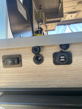 RV rental interior showing coach battery switch, 12V power point, and dual USB charging ports. Sink area above.