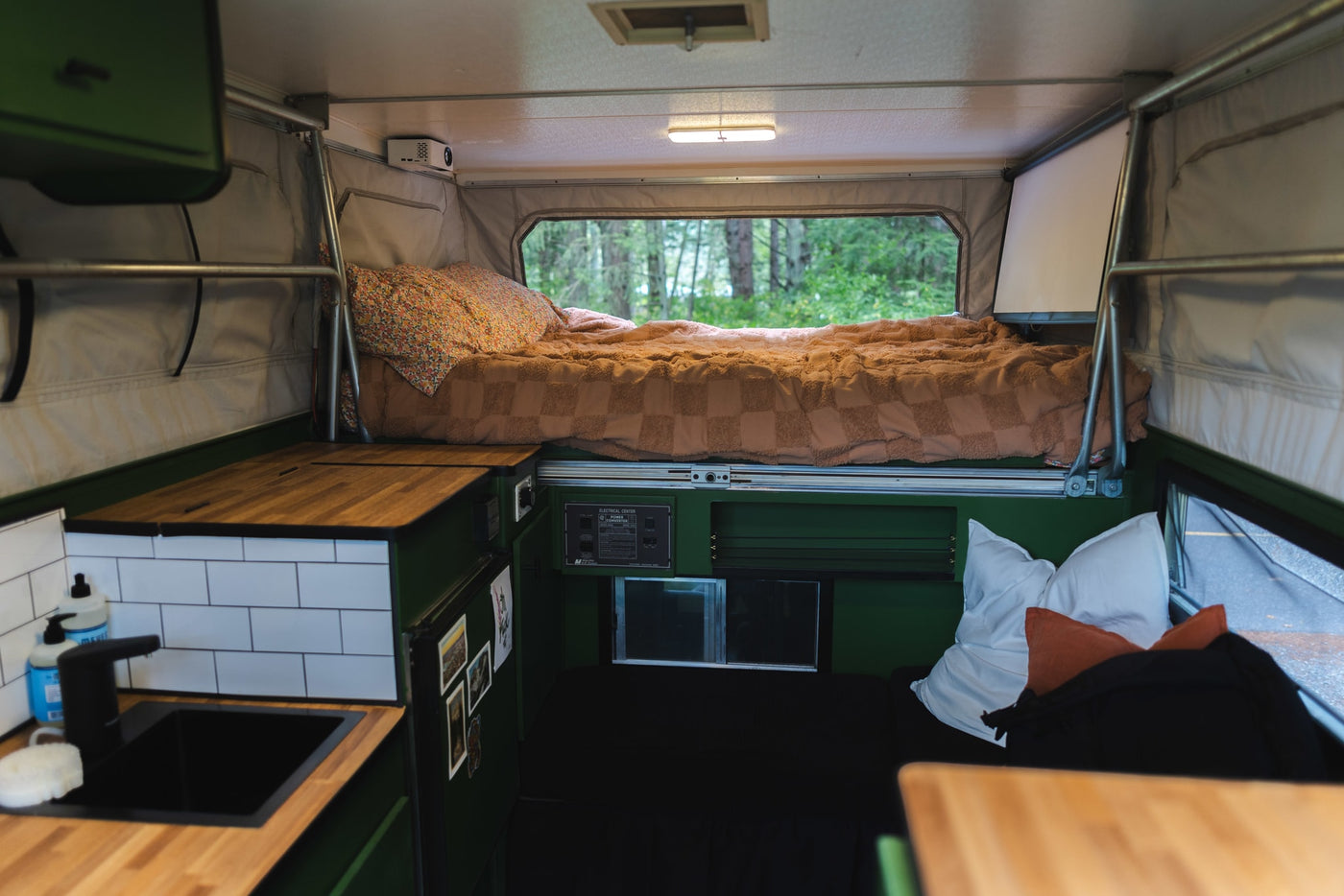 Inside a unique rv rental: cozy elevated bed, kitchen with sink, projector, & forest views. — photo 5