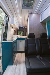Modern RV rental interior with a compact kitchen, passenger seating, and a cozy sleeping area. Features sleek design and wood accents.