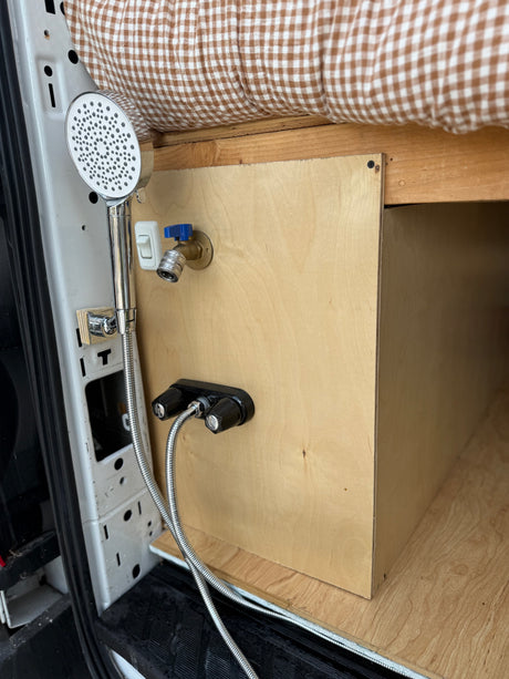 Compact RV rental shower setup: handheld shower, hot/cold mixer, and quick-connect spigot in van interior.