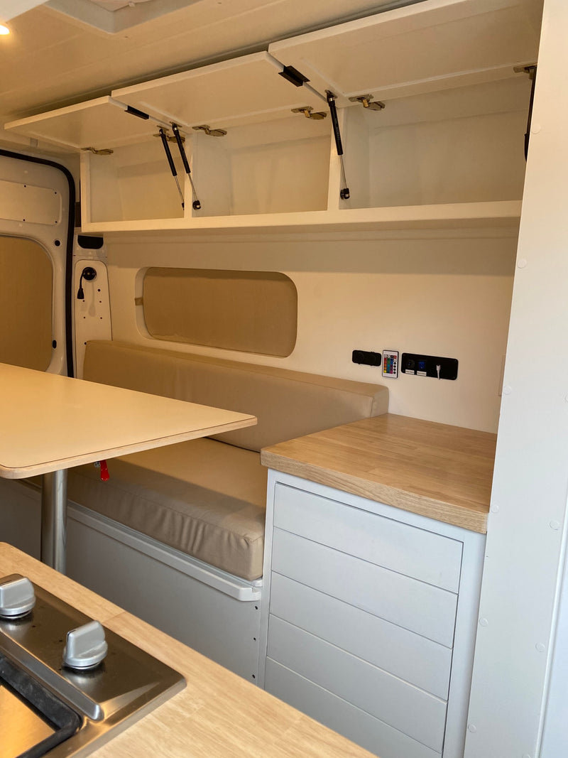 RV rental: well-appointed camper van interior showing kitchen, dining table, cushioned seating, and overhead storage. — photo 11