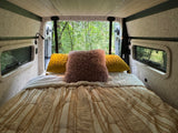 Step into comfort with this RV rental's bed, offering lush forest views from open back doors. Perfect for nature trips.