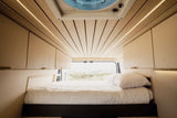 Experience van life! This modern RV rental interior features a cozy bed, wood ceiling with lighting, storage, and a scenic view.