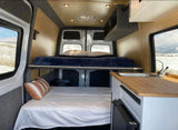 Cozy rv rental van interior featuring bunk beds, a compact kitchen, and windows showing a snowy landscape.