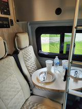 Compact RV rental interior featuring quilted seats and a dining table with disposable items, ready for your travel adventures.
