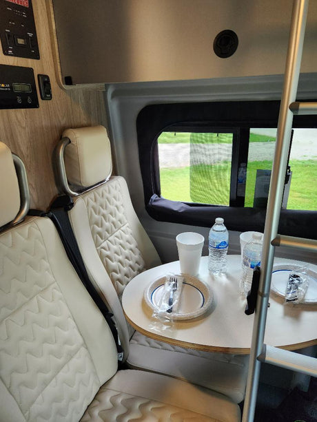 Compact RV rental interior featuring quilted seats and a dining table with disposable items, ready for your travel adventures.