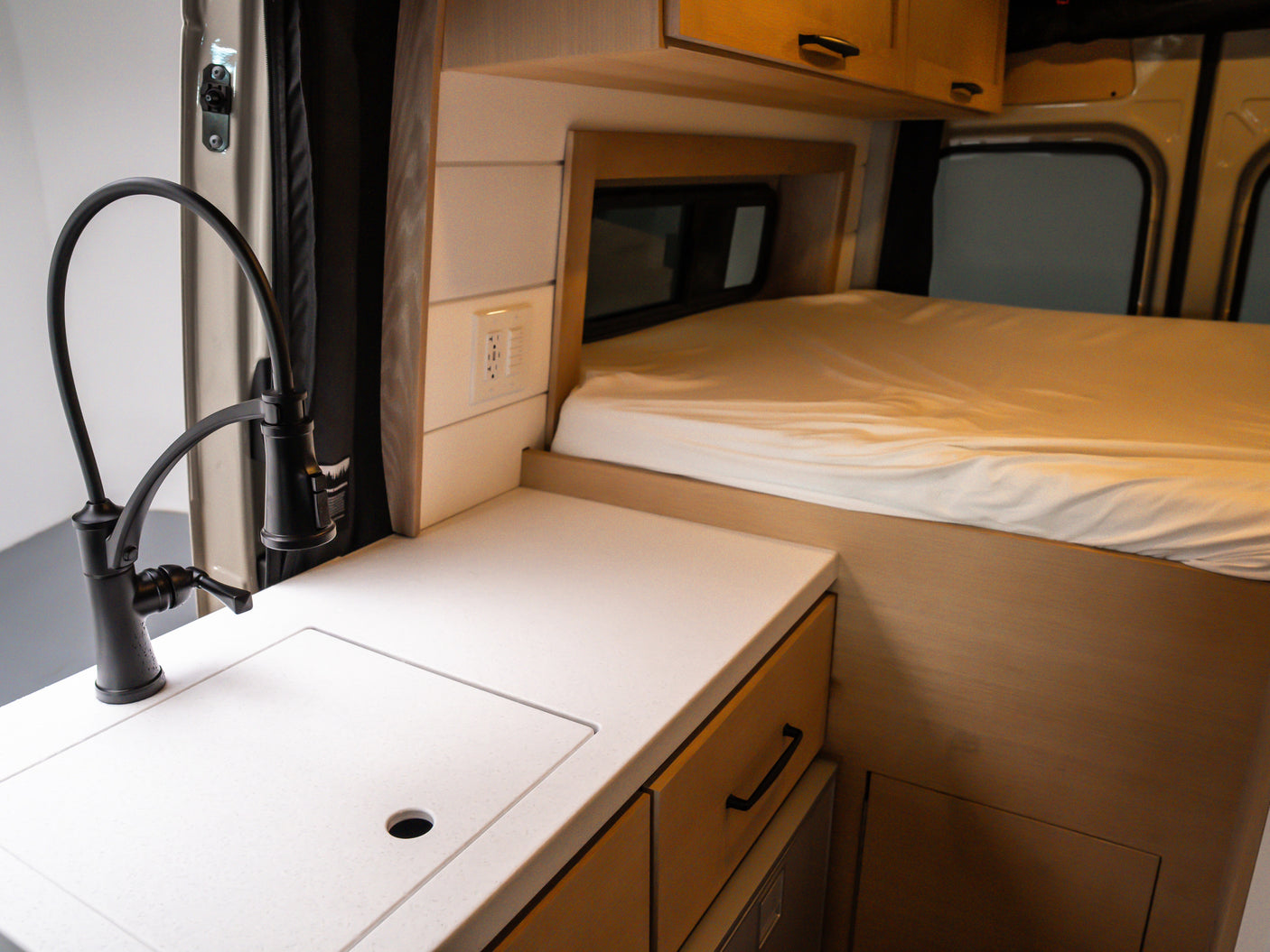 Cozy RV rental interior: A compact kitchen with a black faucet, sink, light-colored countertop, and a neatly made bed.