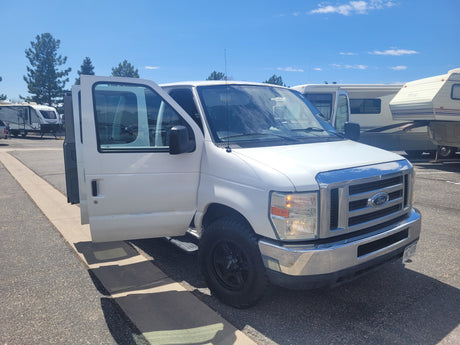 Bright white Ford van with open doors parked among various RVs under blue skies. Ideal rv rental for adventure travel.