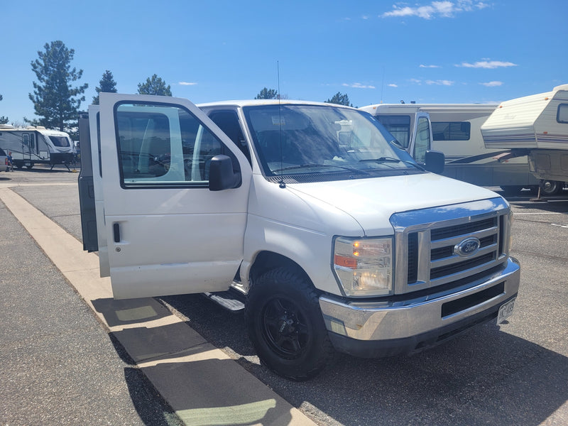 Bright white Ford van with open doors parked among various RVs under blue skies. Ideal rv rental for adventure travel. — photo 8